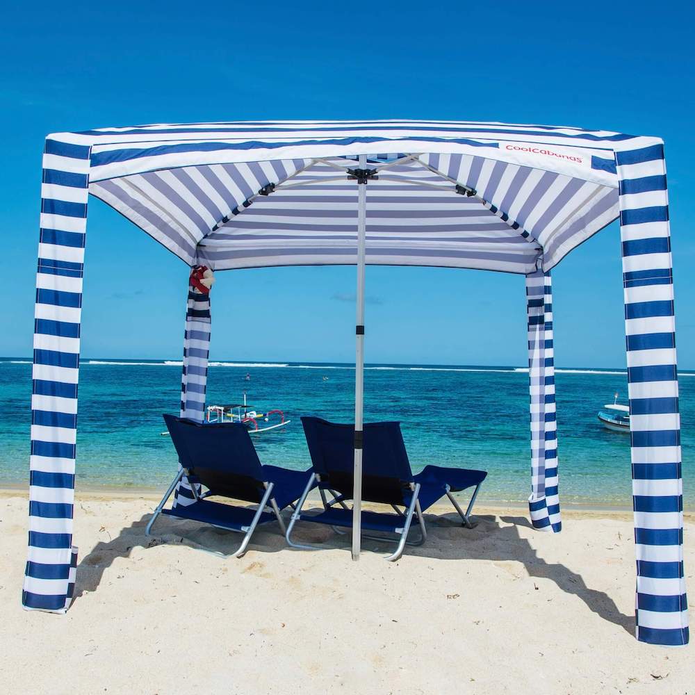 Blue and white striped canopy with two chairs on a sandy beach.