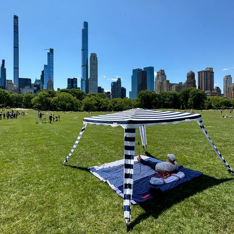 Person lying on a blanket under a striped canopy with a city skyline in the background