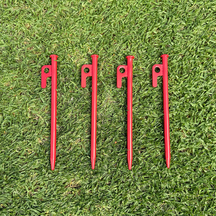 Four red tent stakes on a grassy surface