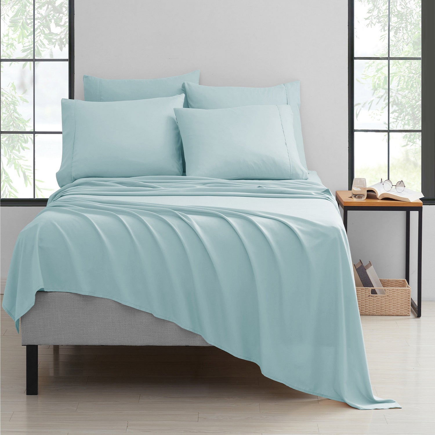 Teal bedding set on a bed in a bright room with large windows.