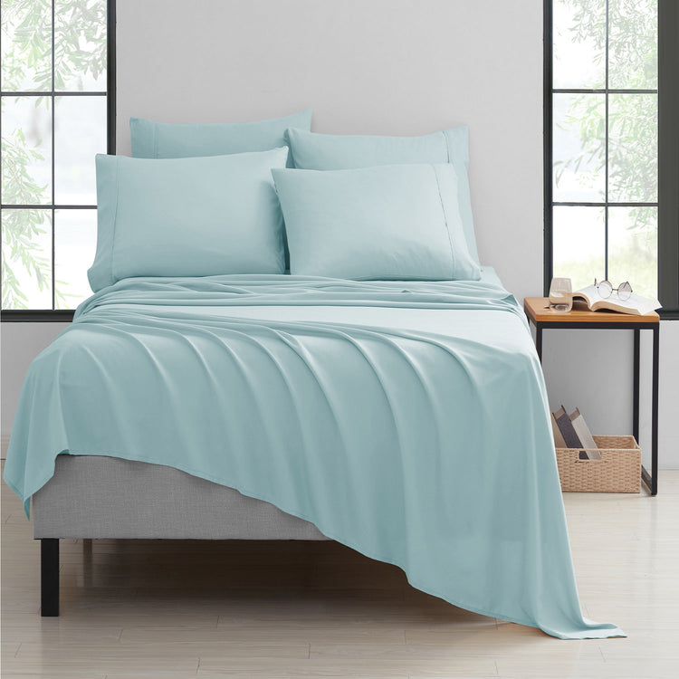 Teal bedding set on a bed in a bright room with large windows.