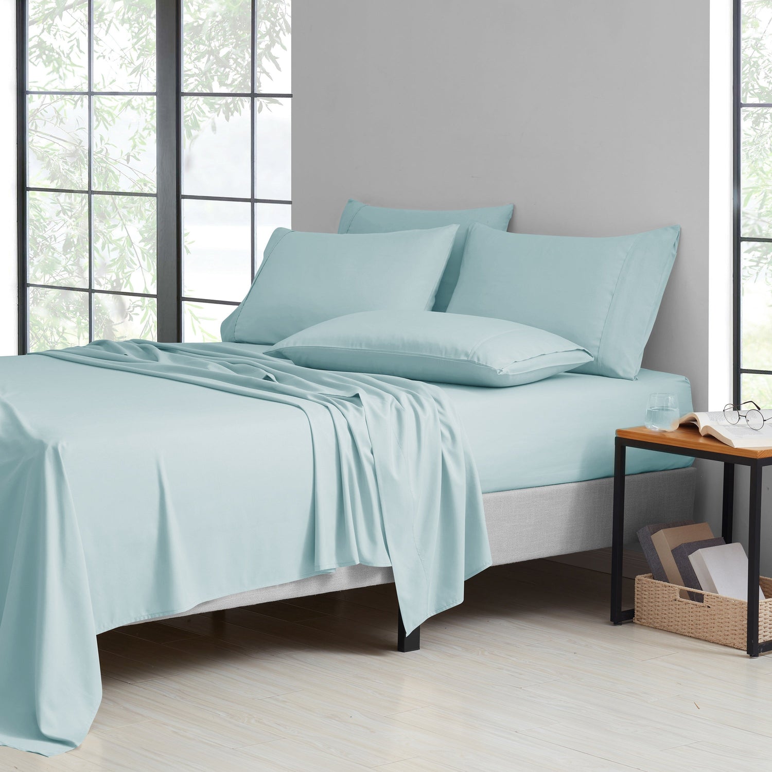 Teal bedding set on a bed in a room with large windows.