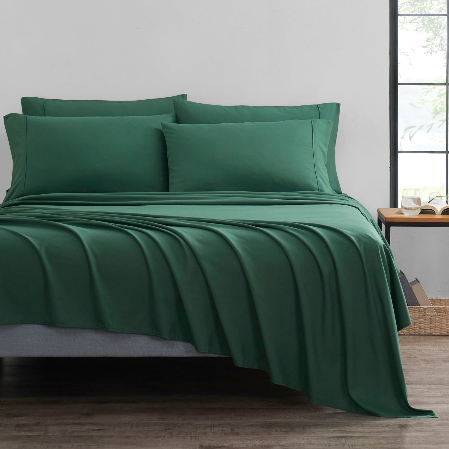 Green bed sheets and pillows on a bed in a room with a window.