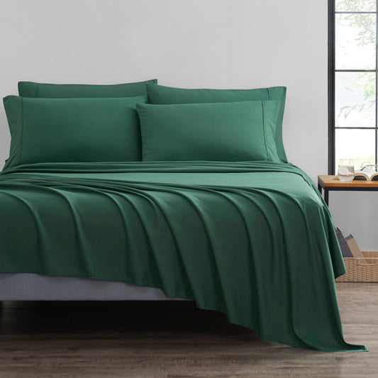 Green bed sheets and pillows on a bed in a room with a window.