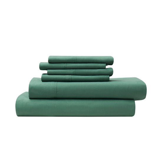 Green bed sheets and pillows on a bed in a room with a window.