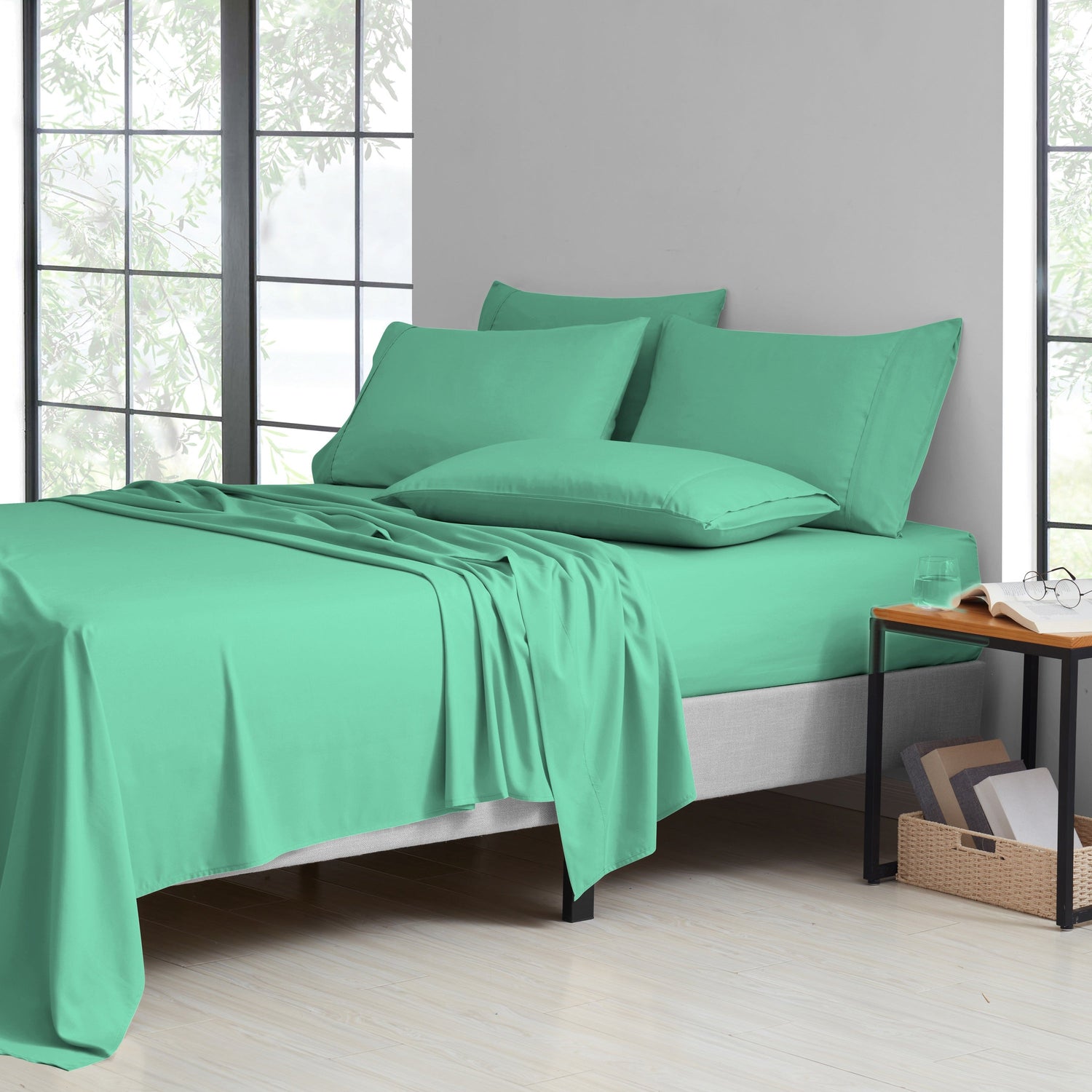 Green bedding set on a bed in a room with large windows.