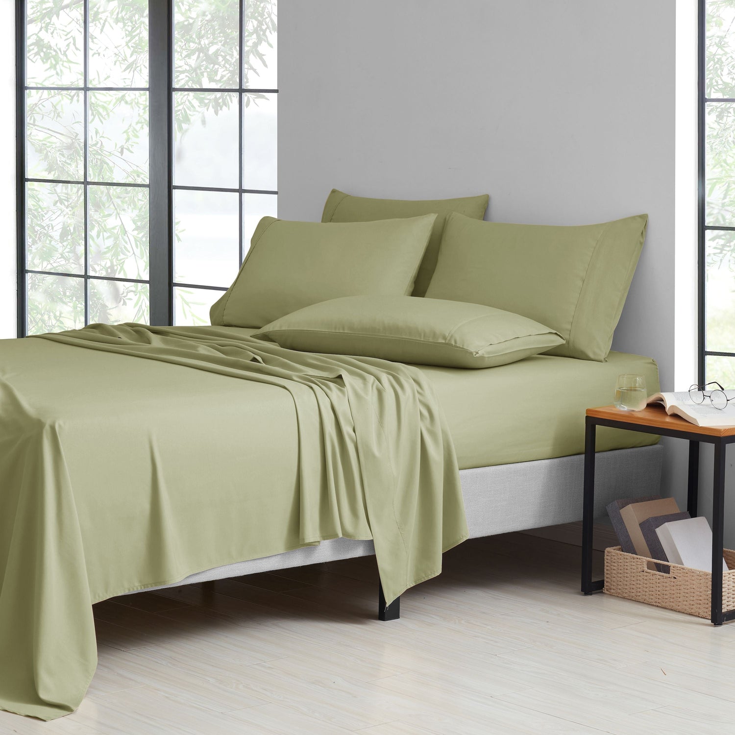 Green bedding set on a bed in a room with large windows.