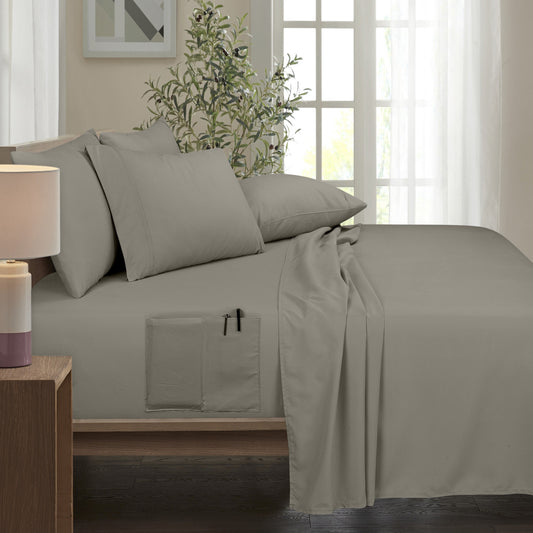 Bed with gray bedding and pillows in a room with large windows.
