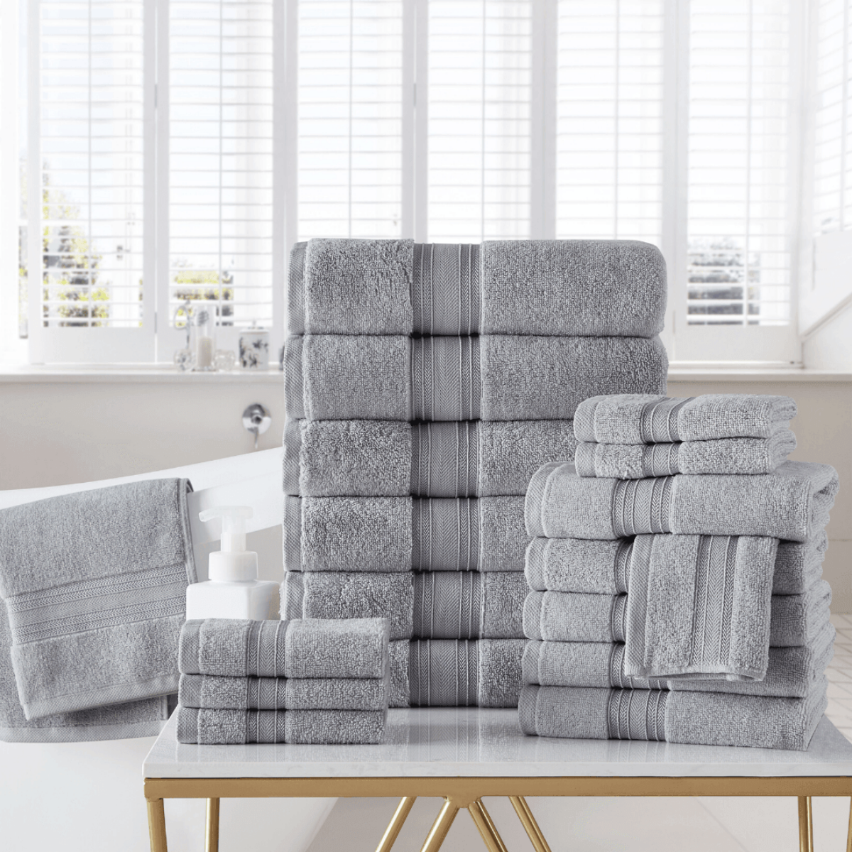 Stack of gray towels with striped patterns on a white surface in a bright room.