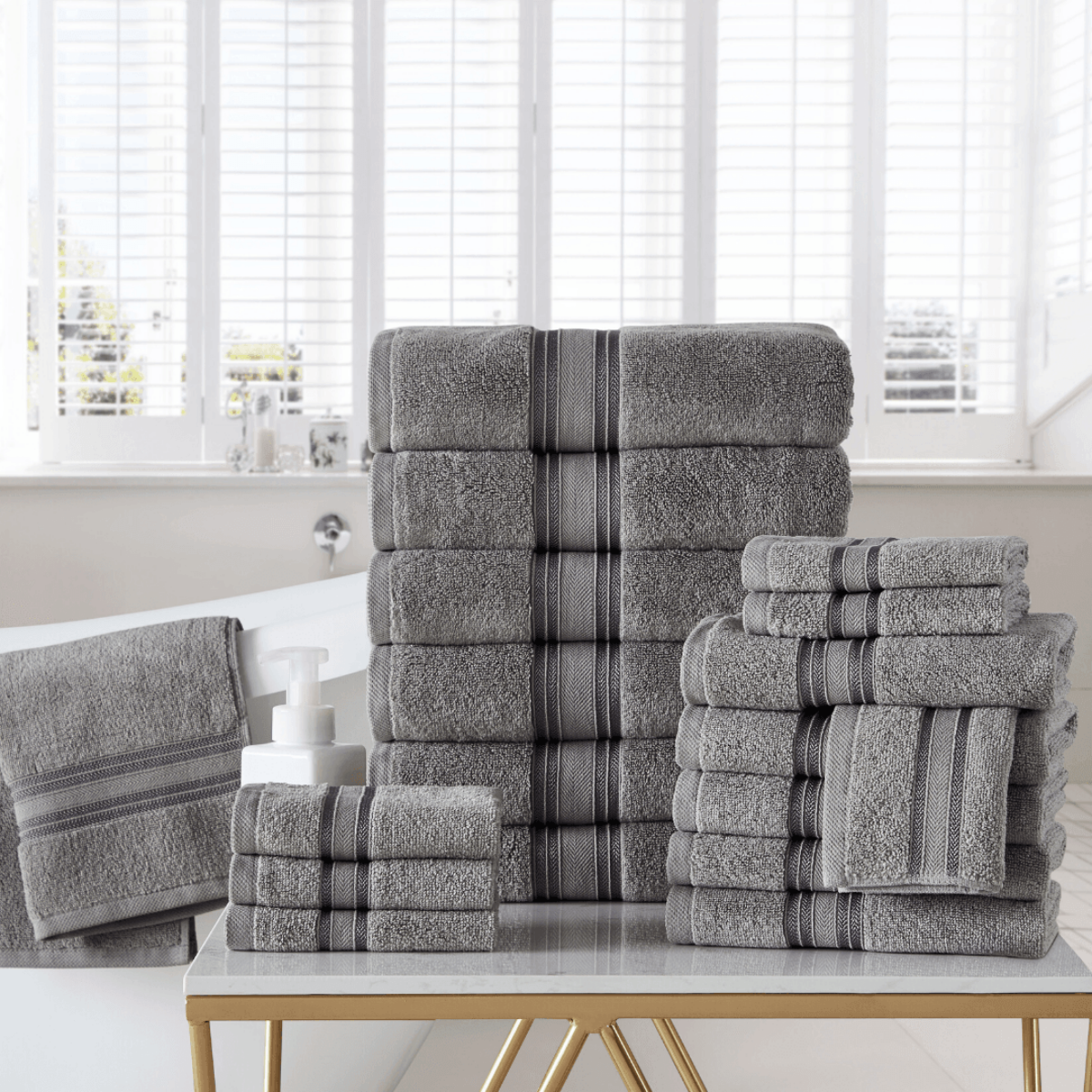 Stack of gray towels with striped patterns on a table in a bright room.