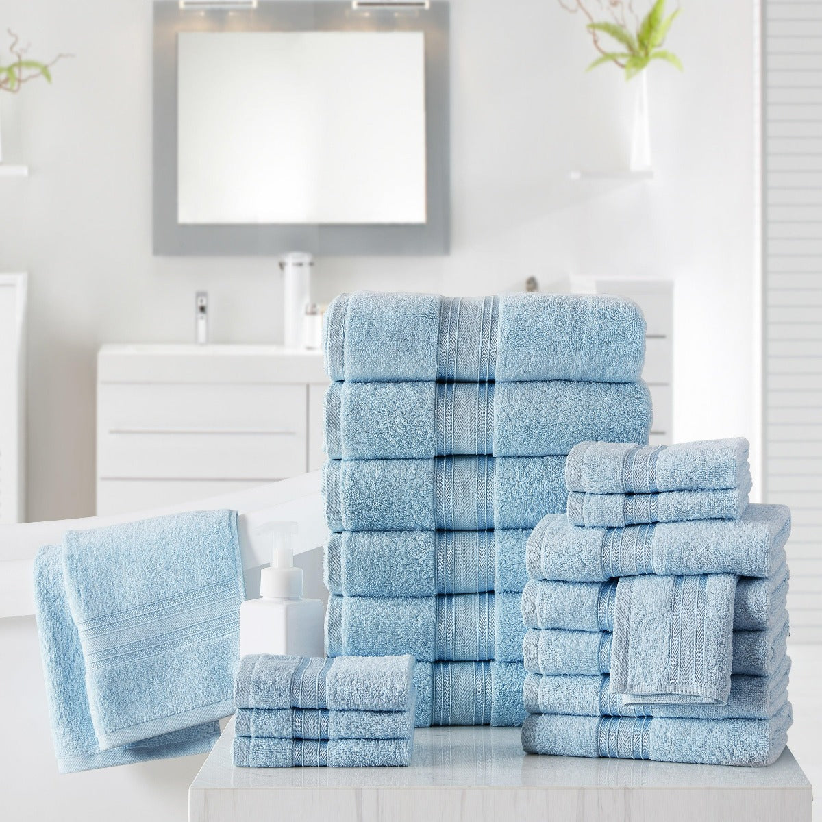 Set of light blue towels on a white surface with a mirror and plant in the background.