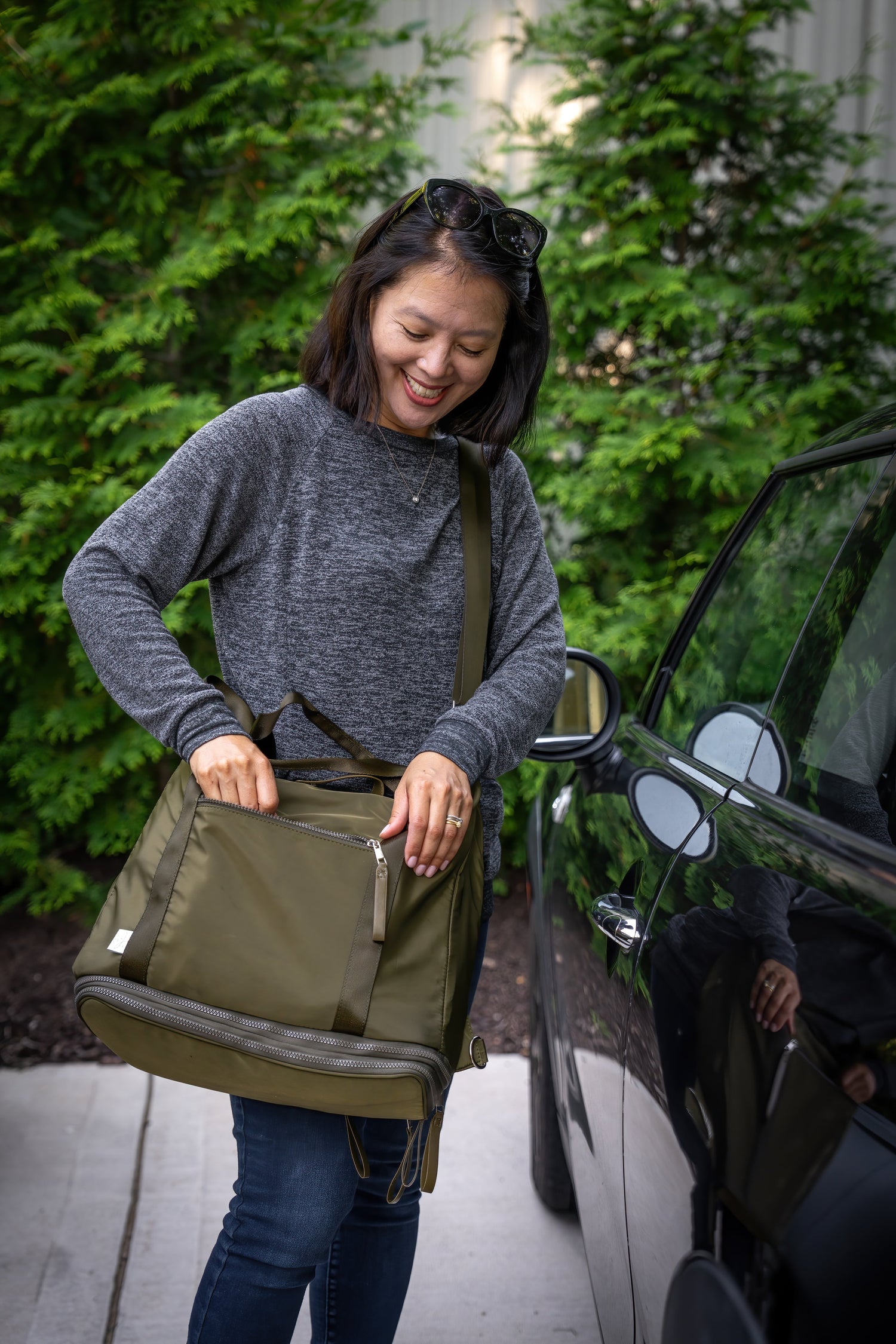 Woman carrying a green bag, getting into a car with greenery in the background