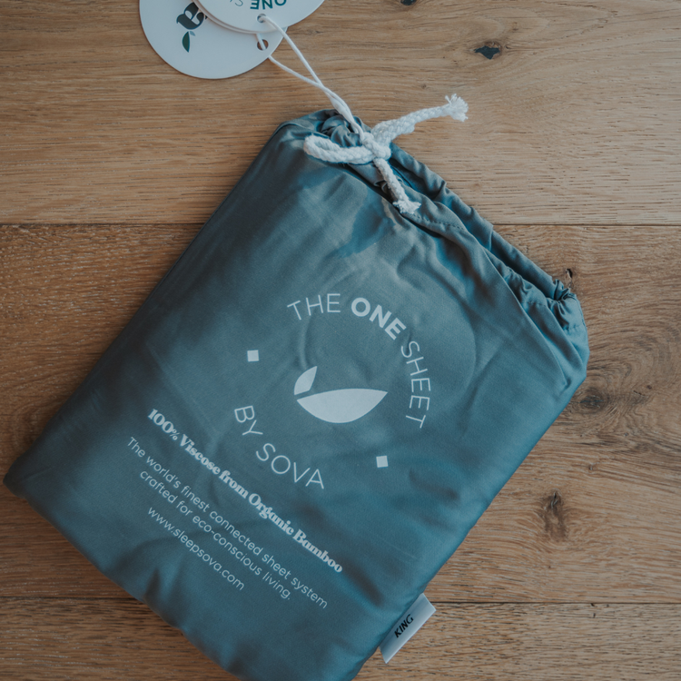 Teal drawstring bag with 'The One Sheet by Sova' branding on a wooden surface