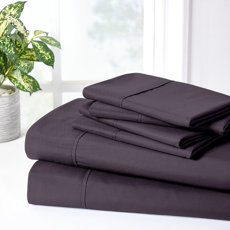Stack of purple bed sheets on a white surface with a plant in the background