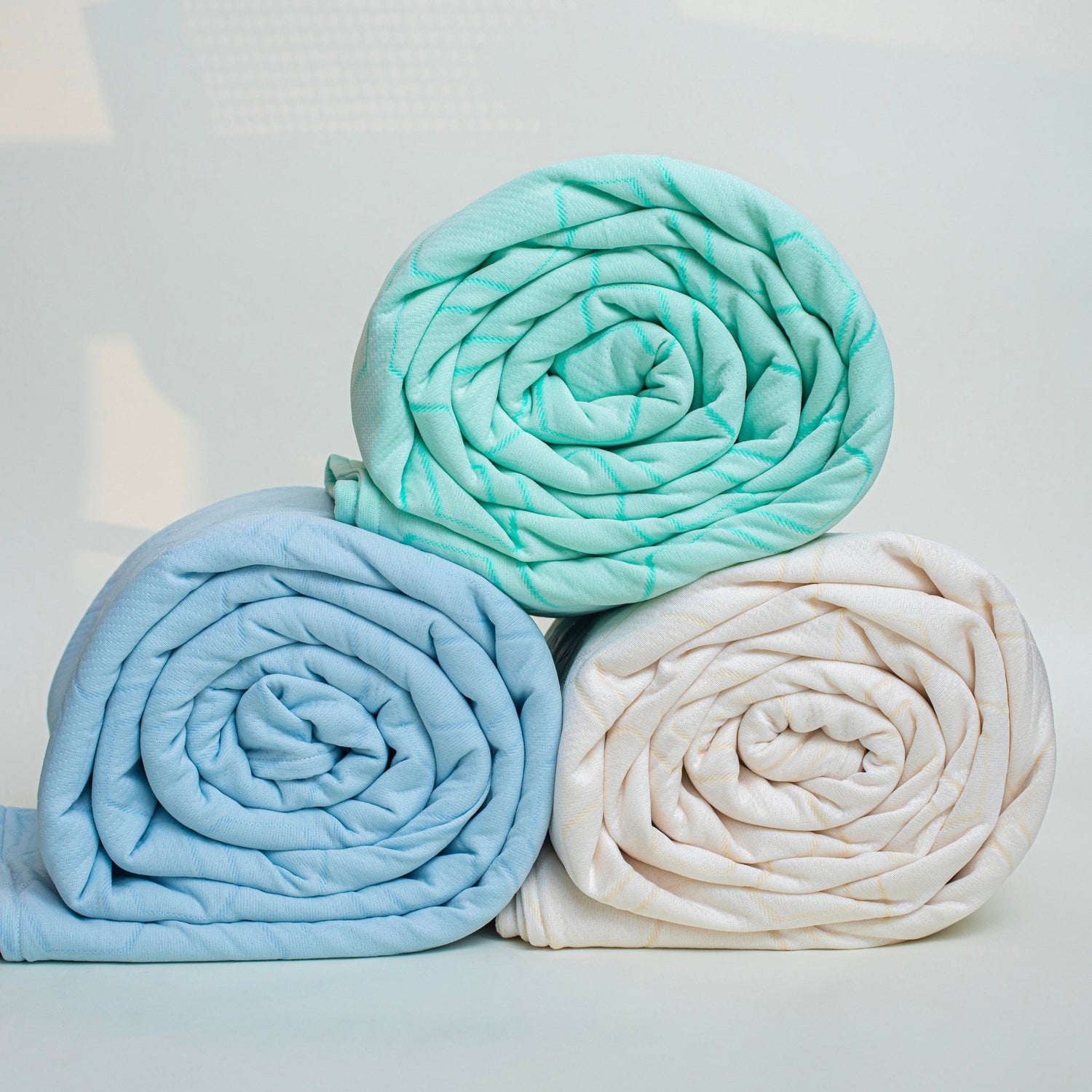 Three rolled-up blankets in teal, blue, and white on a light gray background