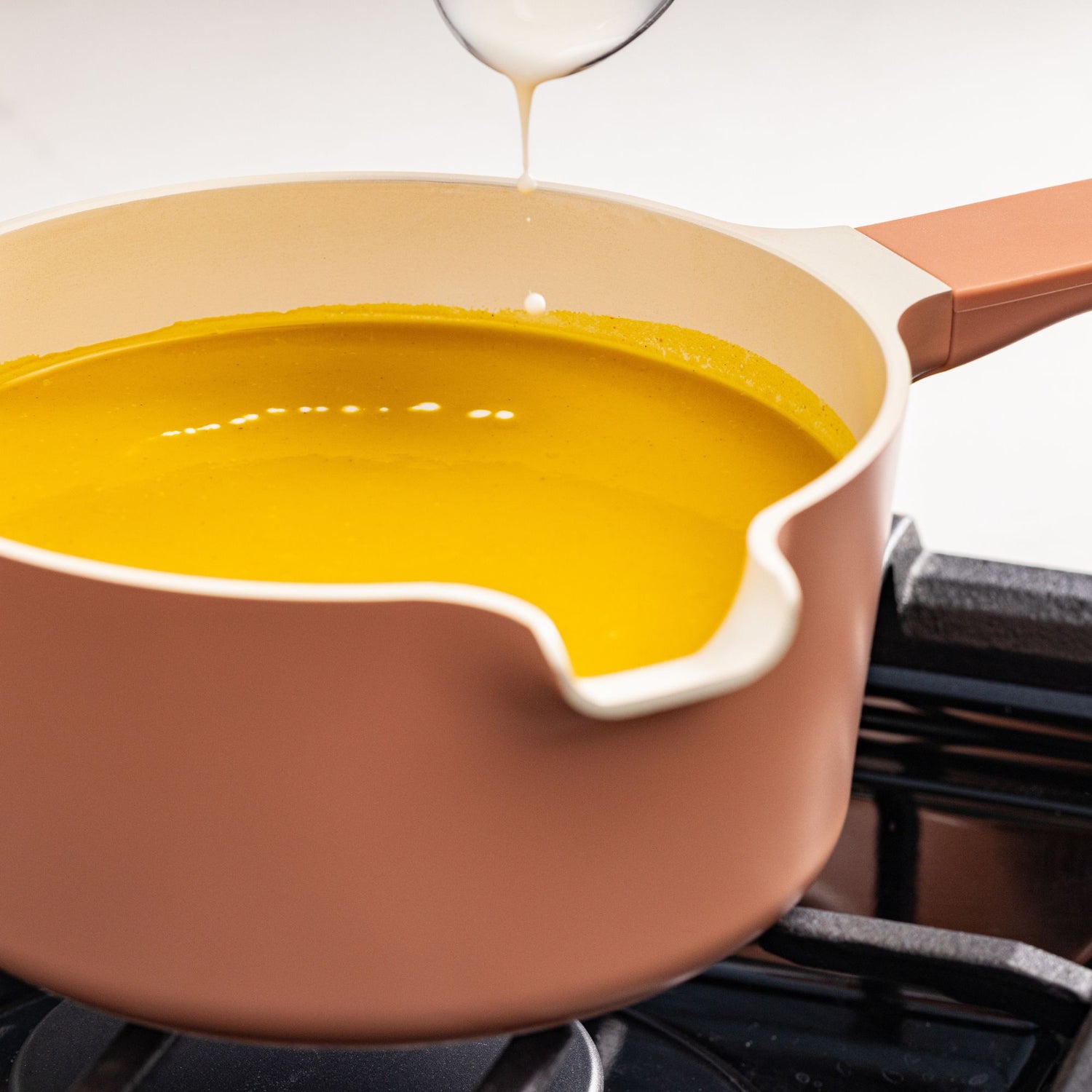 Yellow liquid being poured into a beige pot on a stove