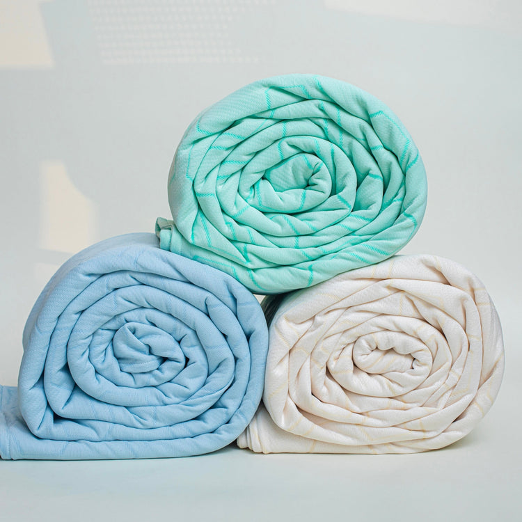 Three rolled-up blankets in teal, blue, and white on a light gray background