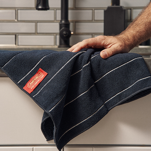 Stack of dark blue towels with white stripes and a red label on a white background