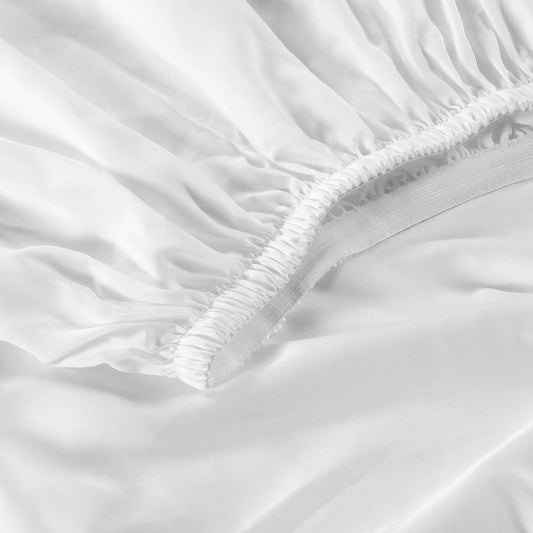 Bed with white bedding and pillows in a room with large windows and wooden side table.