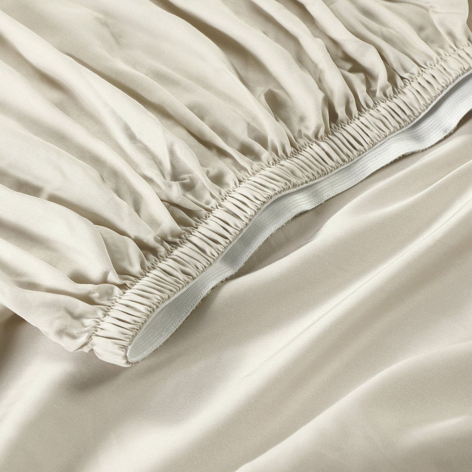 Beige fitted sheet on a bed with a close-up view of the fabric and elastic band.