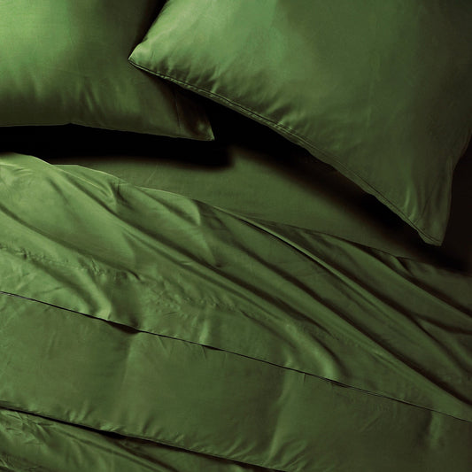 Green bedspread and pillows on a bed in a room with large windows.