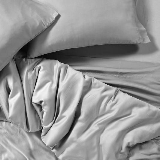 Neatly made bed with beige bedding in a room with large windows.