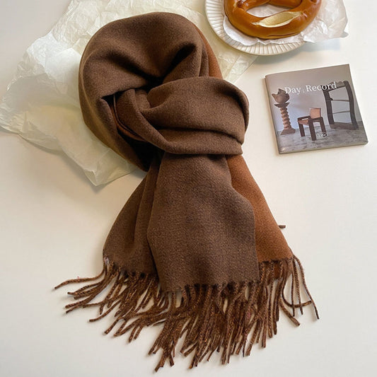 A green reversible pashmina scarf with fringe detailing, displayed on a white surface next to a beige coat and a pretzel.