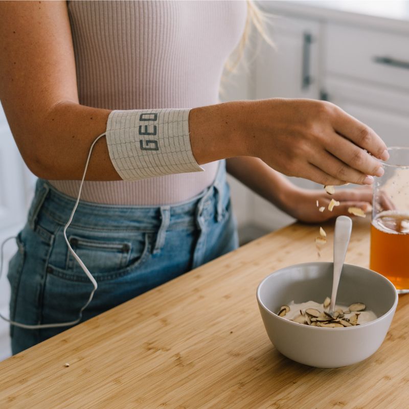 Person pouring cereal into a bowl on a wooden table with a GEQ band on their arm.