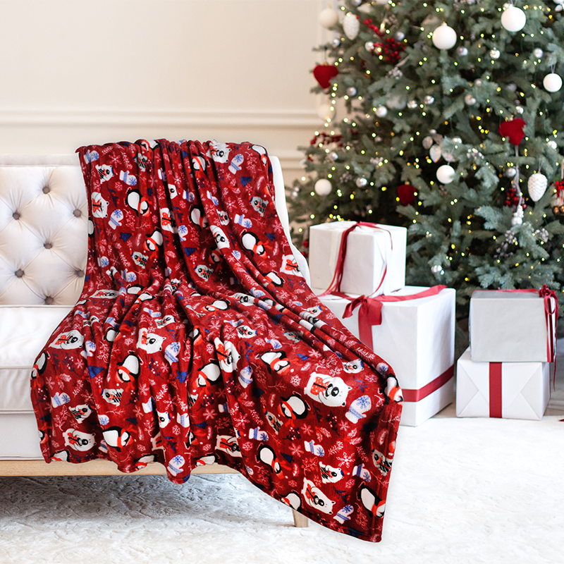 Red Christmas-themed blanket draped over a chair with a decorated Christmas tree and presents in the background.