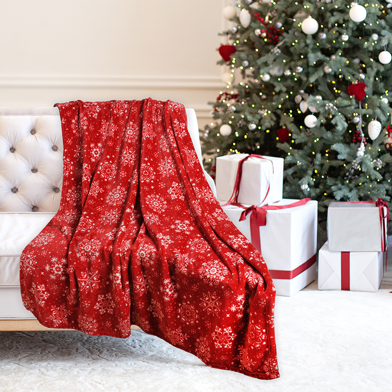 Red floral-patterned blanket draped over a chair with a Christmas tree and presents in the background.