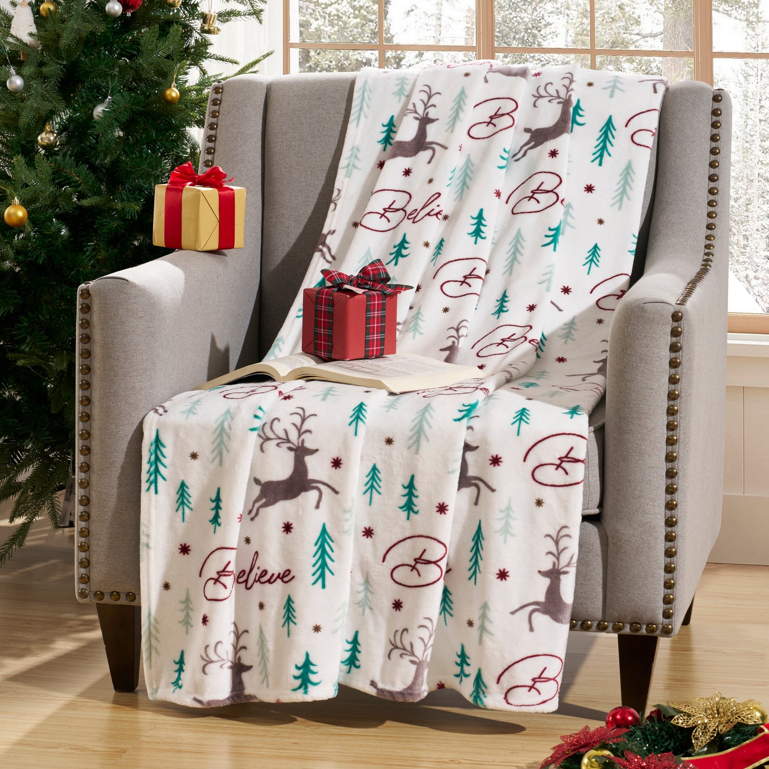 Christmas-themed blanket with reindeer and trees on a chair next to a decorated tree.