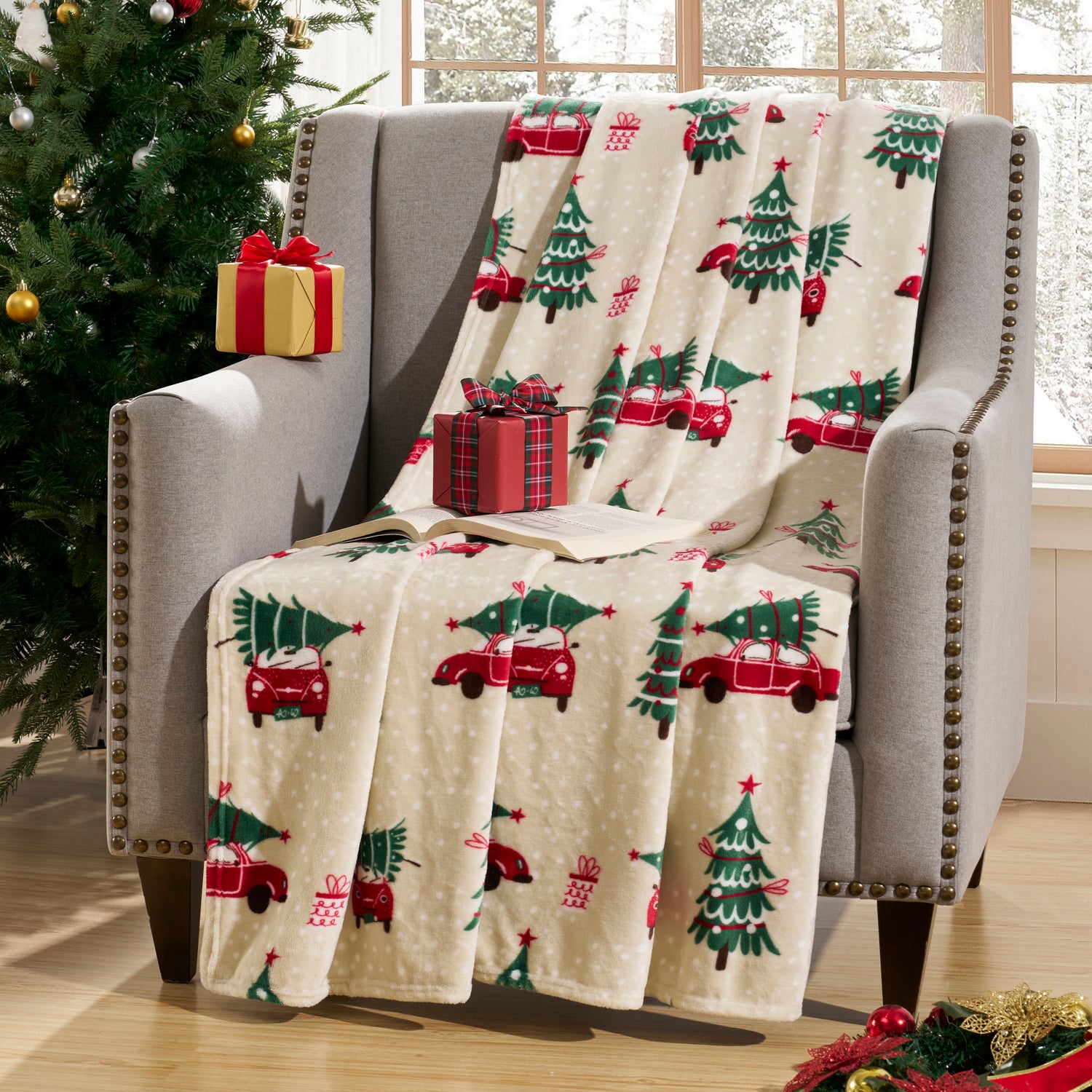 Christmas-themed blanket with red trucks and green trees draped over a chair next to a decorated Christmas tree.