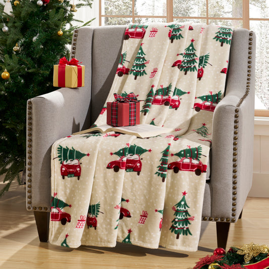 Christmas-themed blanket with red trucks and green trees draped over a chair next to a decorated Christmas tree.