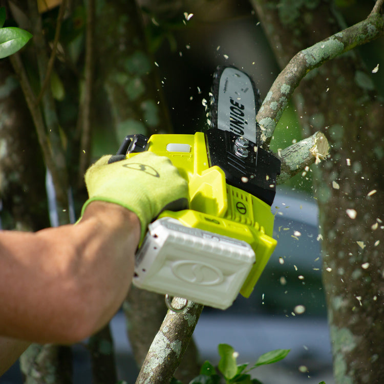 Person using a yellow chainsaw to trim branches in a garden setting