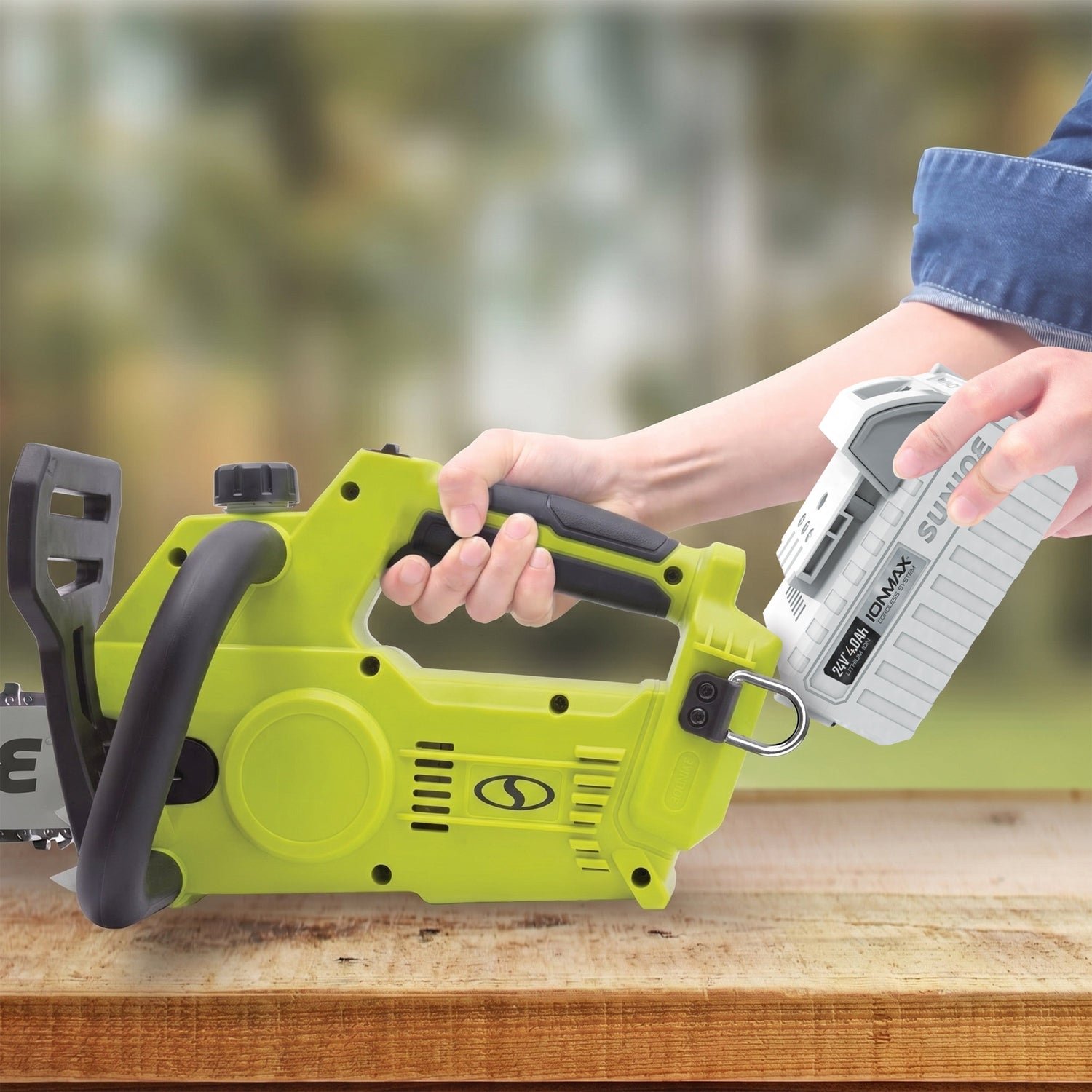 Person holding a green power tool on a wooden surface with a blurred natural background