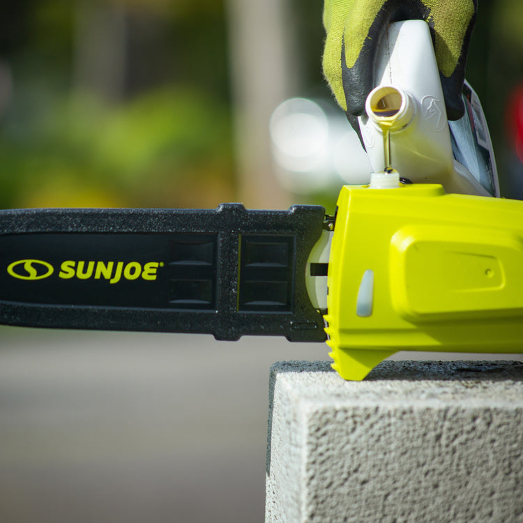 Sun Joe chainsaw on a concrete block with a blurred green background