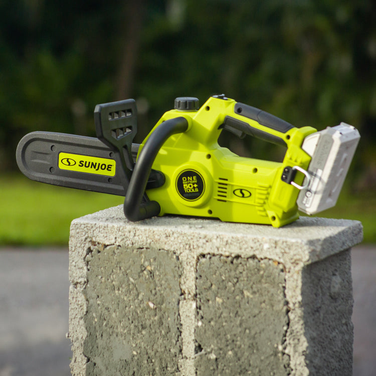 Green chainsaw with black accents on a concrete block against a blurred natural background