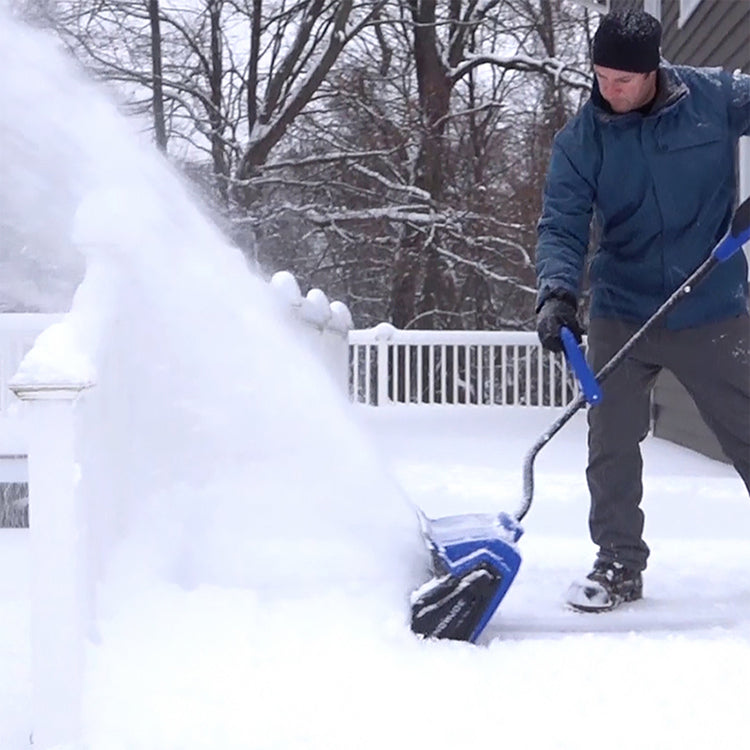 Person using a snow shovel to clear snow from a driveway on a snowy day.