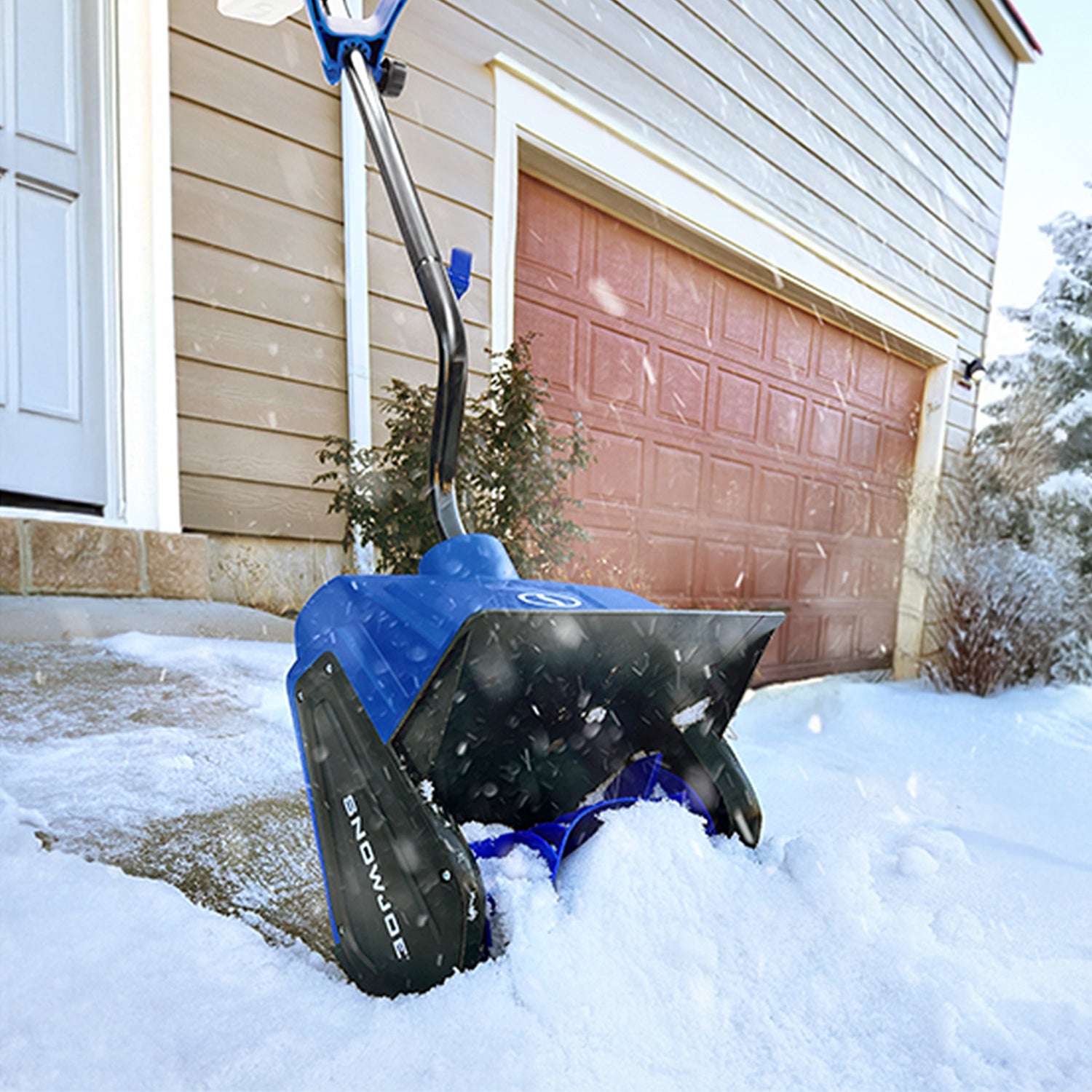 Blue snow shovel being used to clear snow in front of a garage.