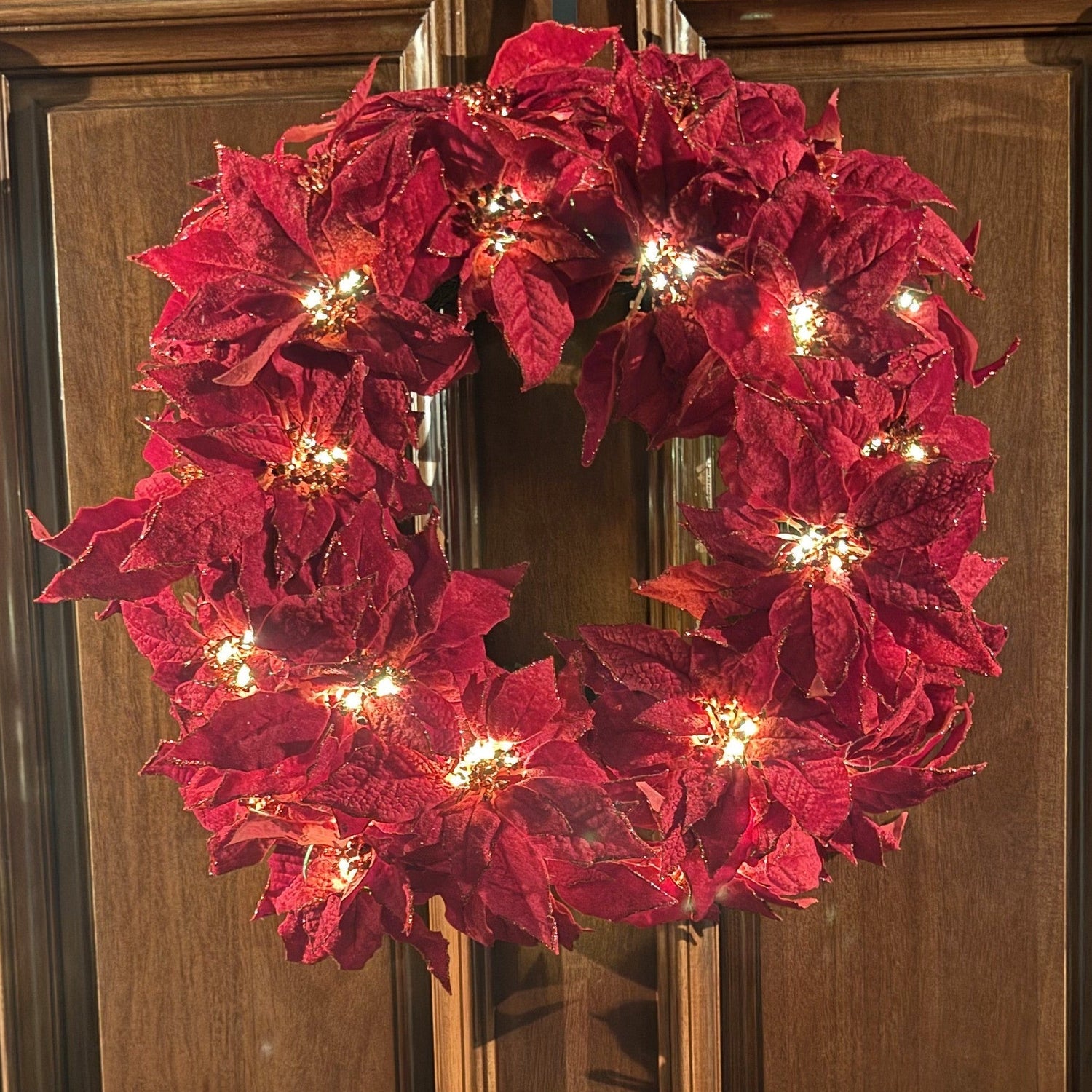 Red poinsettia wreath with lights on a wooden door