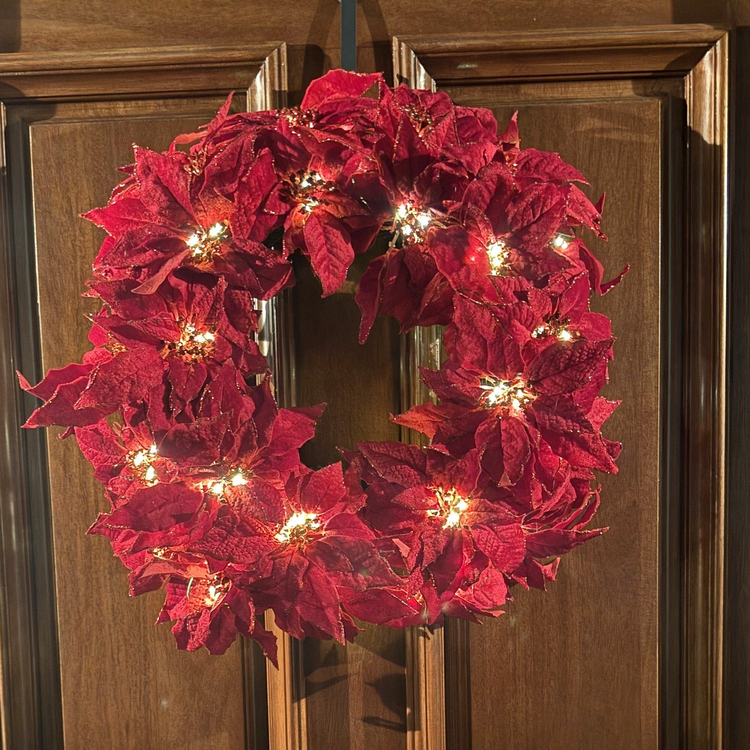 Red poinsettia wreath with lights on a wooden door