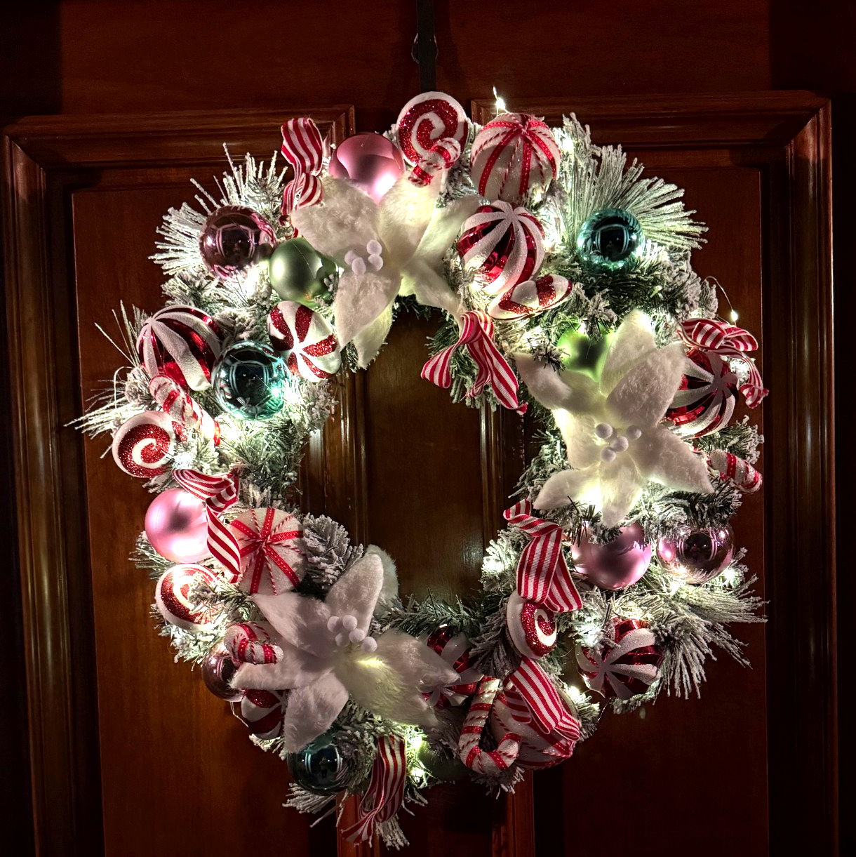 Decorative Christmas wreath with candy-themed decorations on a wooden door.