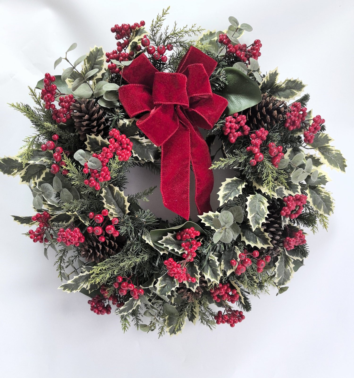 Christmas wreath with red berries, pine cones, and a red bow on a white background
