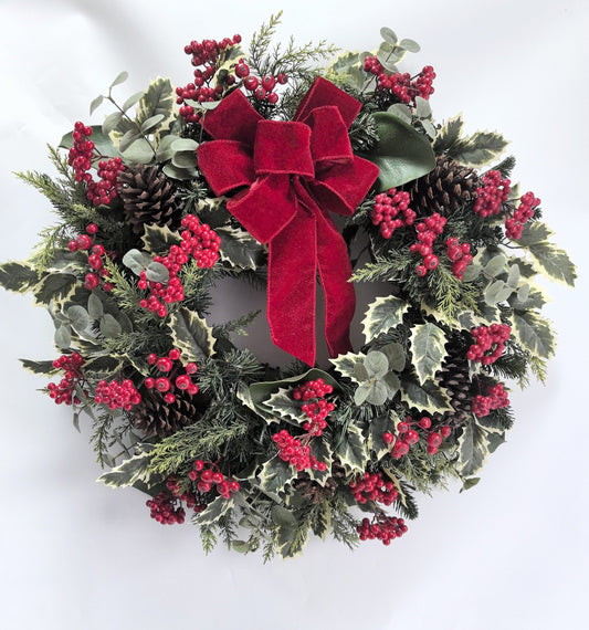 Christmas wreath with red berries, pine cones, and a red bow on a white background