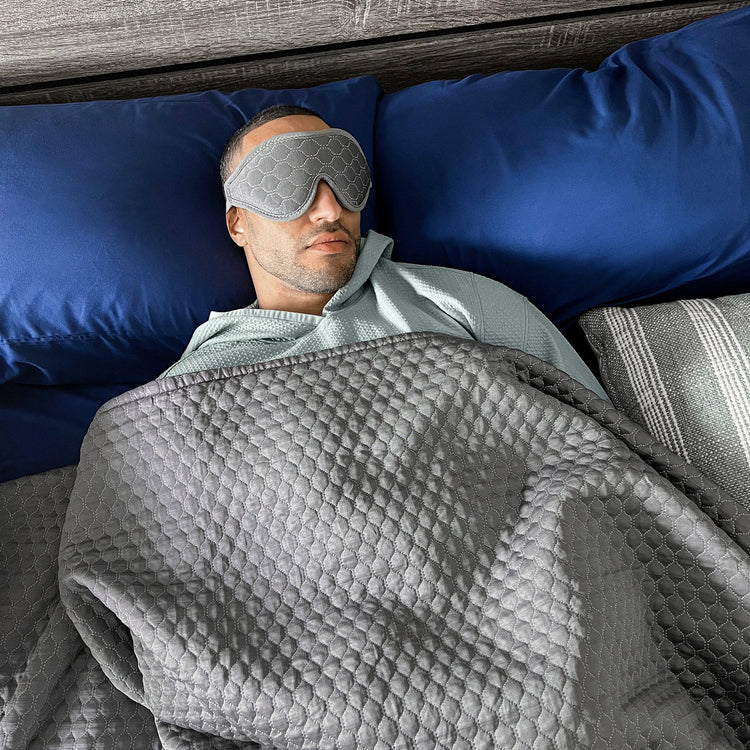 Man lying in bed with a gray eye mask and blanket