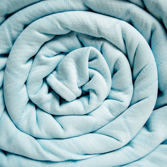 Light blue textured bedspread and pillowcases on a wooden bed in a bedroom setting.