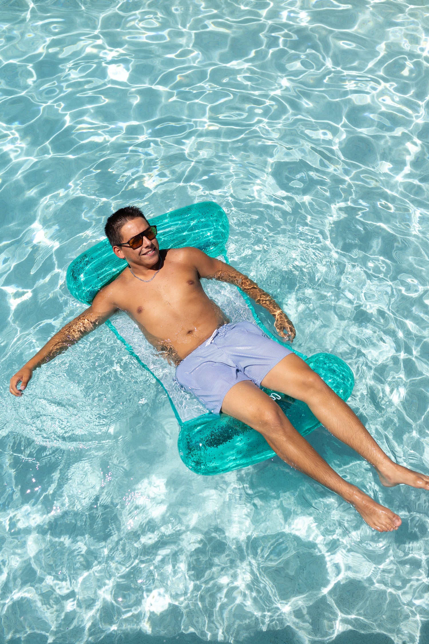 Man lying on a clear inflatable raft in clear blue water