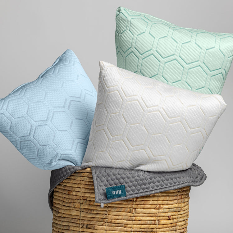 Three textured pillows in blue, white, and green on a wicker basket with a gray background.