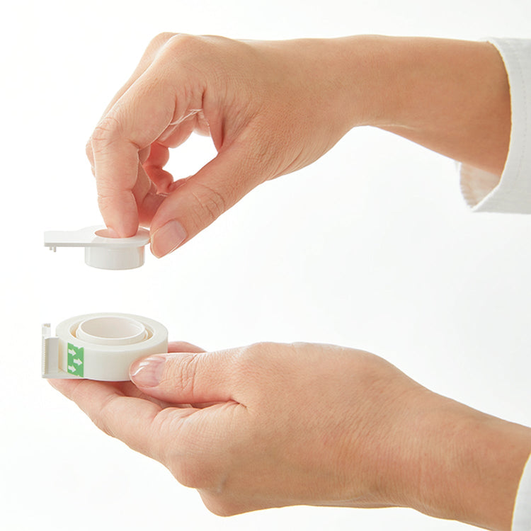Person holding a roll of white tape with a small container on a white background