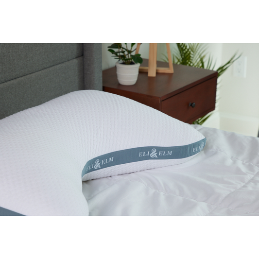 A white, rectangular side sleeper pillow with a pillowcase on a bed, against a wooden headboard background.